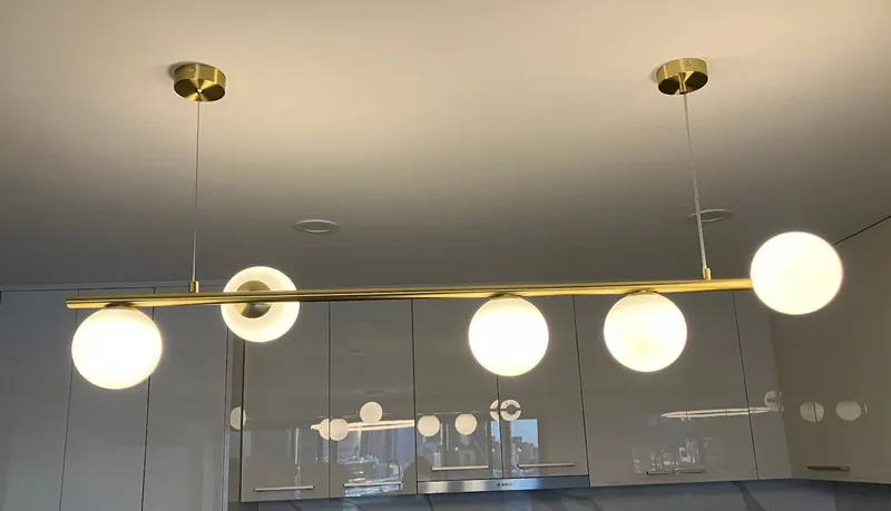 Brass linear pendant light with glass globes above a kitchen