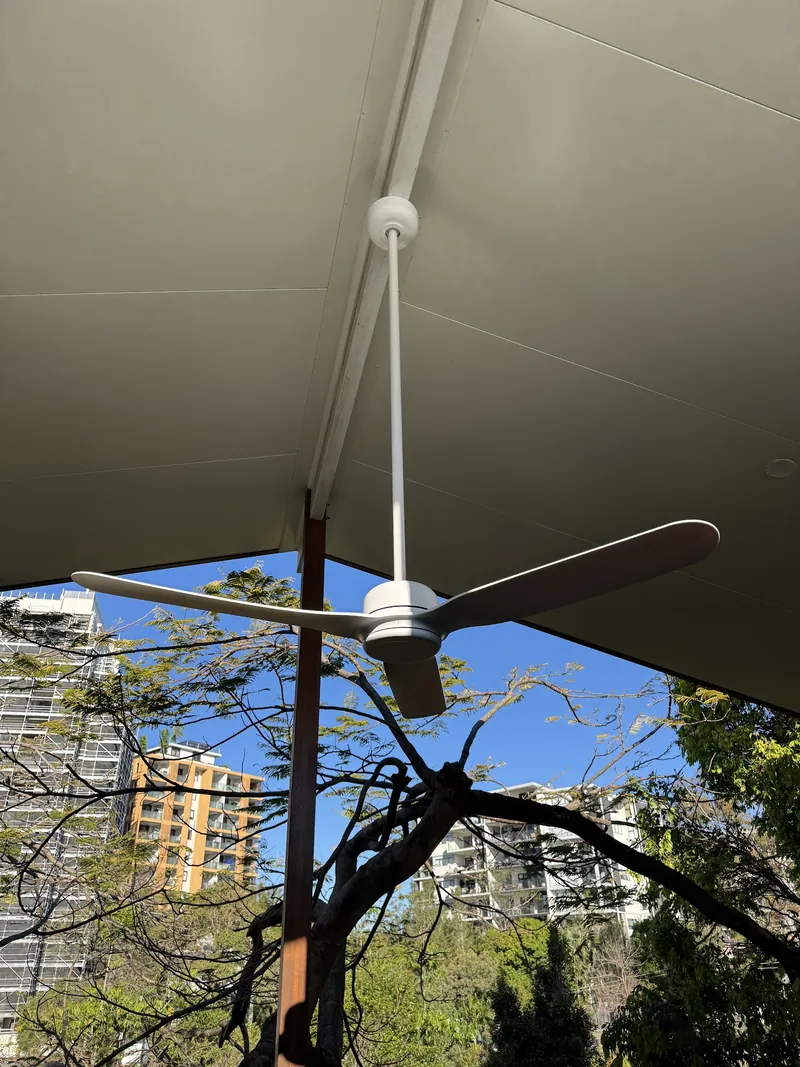 Outdoor ceiling fan on a covered patio overlooking trees and the city